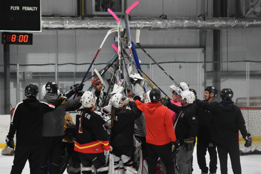 A group of coaches and goalies hold their sticks up in the air.
