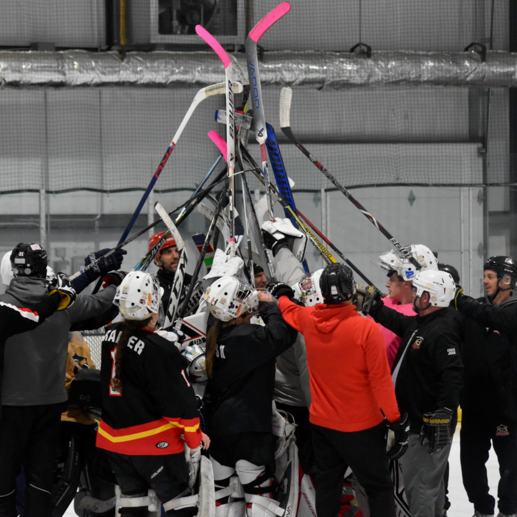 A group of coaches and goalies hold their sticks up in the air.