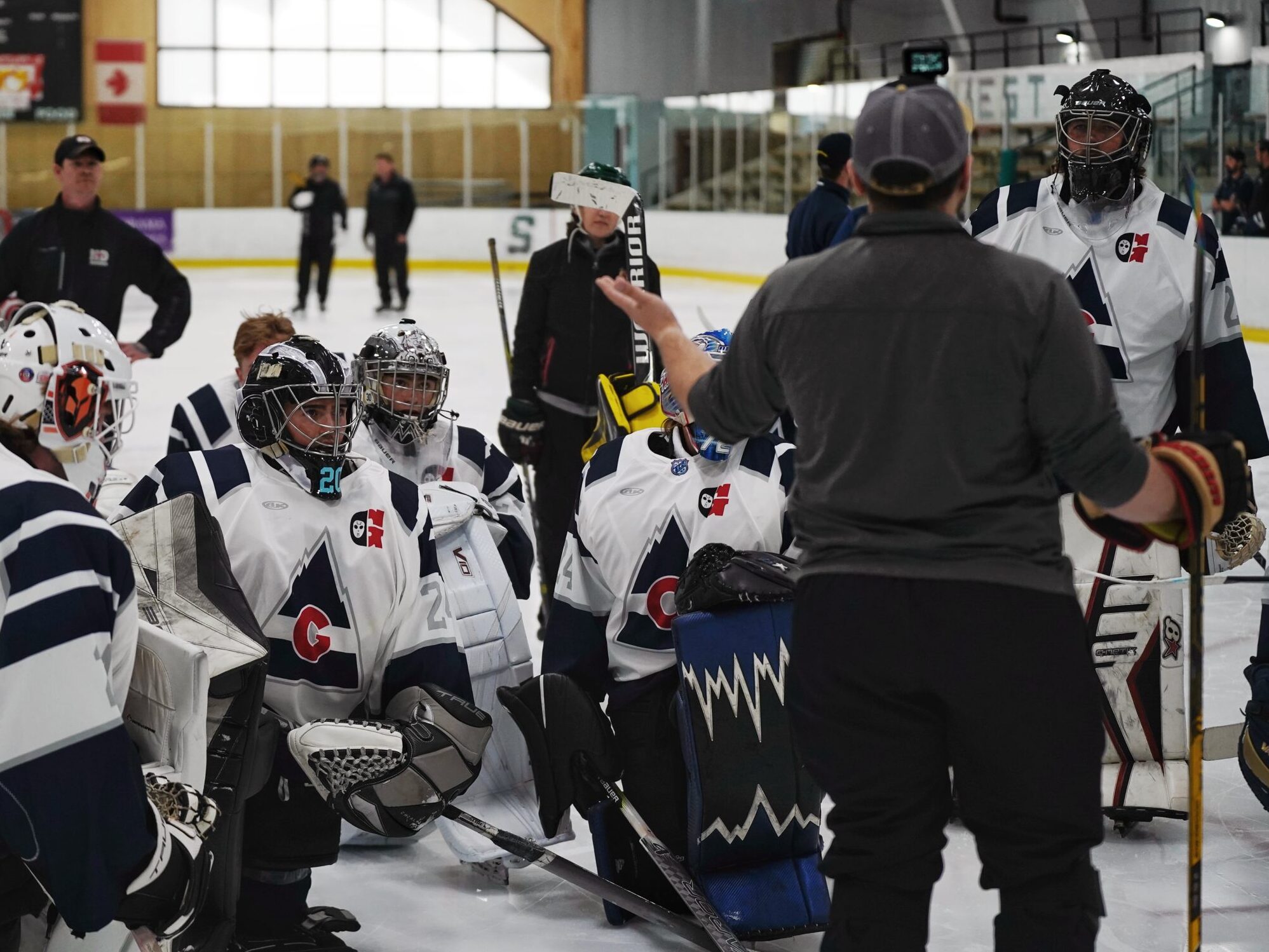 A coach speaks to several hockey goaltenders.