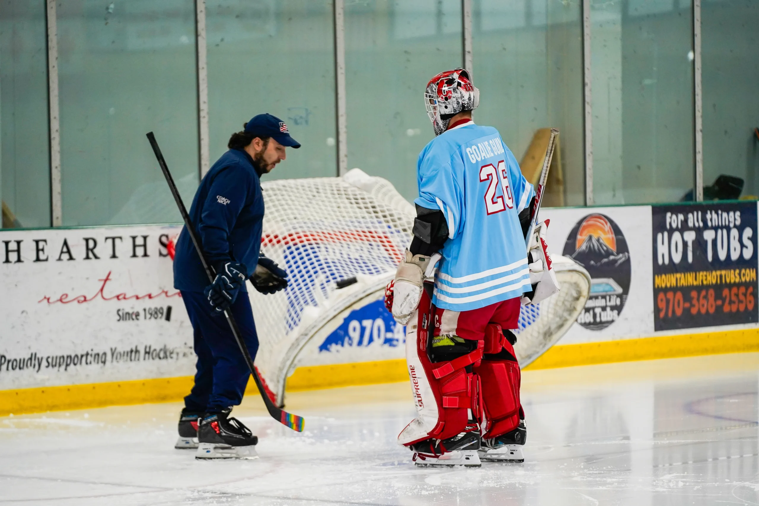 A coach demonstrating skating technique to a hockey goalie.